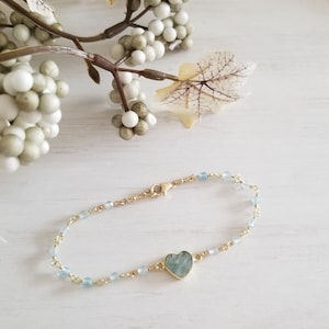 May include: A delicate gold chain bracelet with light blue beads and a heart-shaped aquamarine gemstone pendant.