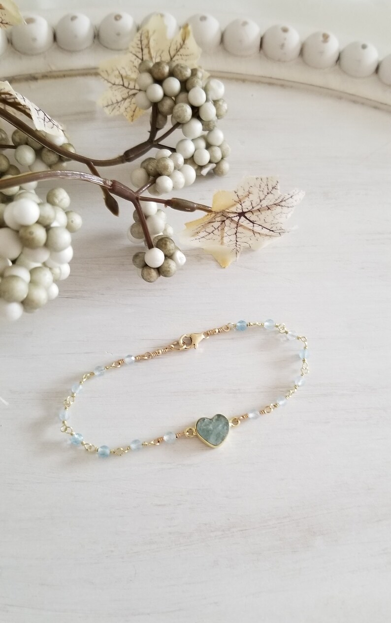 May include: A delicate gold chain bracelet with light blue beads and a heart-shaped aquamarine gemstone pendant.