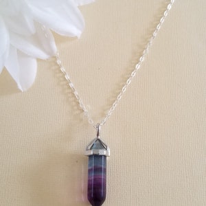 May include: A silver chain necklace with a purple and green crystal point pendant.