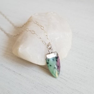 May include: A silver chain necklace with a green and pink gemstone pendant. The pendant is shaped like a teardrop and has a silver setting.