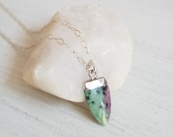May include: A silver chain necklace with a green and pink gemstone pendant. The pendant is shaped like a teardrop and has a silver setting.