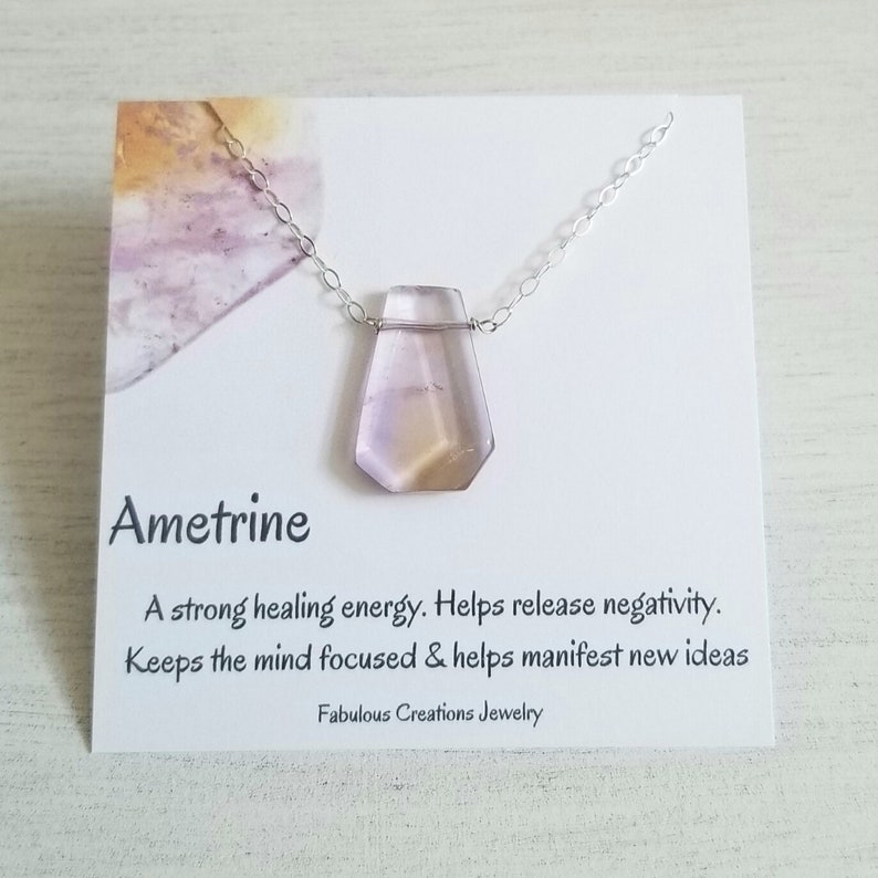May include: Ametrine necklace with a purple and yellow crystal pendant. The card reads: "Ametrine A strong healing energy. Helps release negativity. Keeps the mind focused & helps manifest new ideas Fabulous Creations Jewelry"