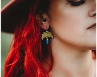 May include: A woman with bright red hair wearing a brown hat and gold earrings with turquoise stones.