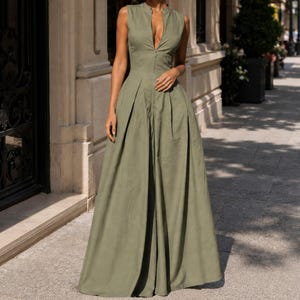 Op de afbeelding: Olijfgroene mouwloze jumpsuit met een hoge kraag en een diepe halslijn. De jumpsuit heeft een getailleerd lijfje met een ritssluiting en wijde pijpen. De stof lijkt een lichtgewicht materiaal te zijn, geschikt voor warmer weer.