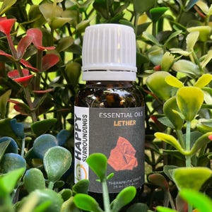 May include: A brown glass bottle of "Lether" essential oil with a white cap. The label reads "Essential Oils" and "Therapeutic Grade 15 ml (0.5 fl oz)". The bottle is set against a backdrop of green, red, and blue foliage.