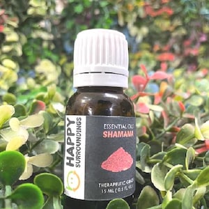 Peut inclure: Une bouteille en verre marron d'huile essentielle avec un bouchon blanc. L'étiquette indique "SHAMAMA" et "THERAPEUTIC GRADE". La bouteille contient 15 ml (0,5 fl oz). L'arrière-plan est un mélange de feuillage vert et rouge.