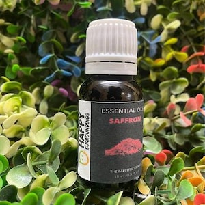 Könnte beinhalten: Eine kleine, dunkle Glasflasche mit ätherischem Safranöl und einem weißen Verschluss. Das Etikett trägt die Aufschrift "Essential Oils Saffron" und "Therapeutic Grade". Die Flasche enthält 15 ml (0,5 fl oz). Der Hintergrund ist eine Mischung aus grünem, gelbem und rotem Laub.