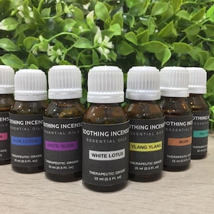 May include: A collection of seven essential oil bottles with white caps and black labels. The labels display the names of the oils: Palmarosa, Blue Lotus, White Musk, White Lotus, Ylang Ylang, Musk, and Tea Tree. Each bottle contains 15 ml (0.5 fl oz) of oil.