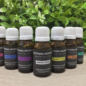 Puede incluir: Una colección de siete botellas de aceites esenciales con tapas blancas y etiquetas negras. Las etiquetas muestran los nombres de los aceites: Palmarosa, Blue Lotus, White Musk, White Lotus, Ylang Ylang, Musk y Tea Tree. Cada botella contiene 15 ml de aceite.