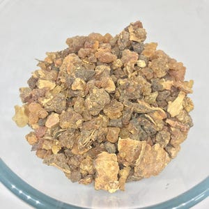 Könnte beinhalten: Eine klare Glasschüssel gefüllt mit einem Haufen bernsteinfarbener, unregelmäßig geformter Stücke. Die Stücke haben eine raue, strukturierte Oberfläche und variieren in der Größe, wobei einige als kleine Brocken und andere als größere Fragmente erscheinen.