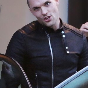 May include: A black leather jacket with a silver zip and white buttons. The jacket features a quilted design on the shoulders. The person in the image is looking towards the camera.