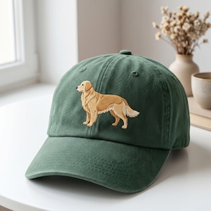 May include: A forest green baseball cap featuring an embroidered golden retriever dog in shades of tan and cream. The cap has a curved brim, a structured crown with ventilation eyelets, and a classic six-panel design with visible stitching.