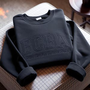 Moletom BCBA bordado, camiseta com fonte universitária para analista comportamental certificado.