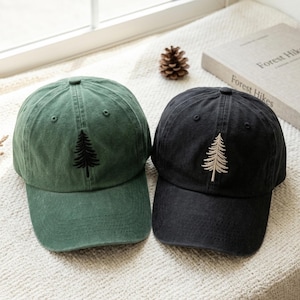 Peut inclure: Deux casquettes de baseball, une vert forêt et une noire, chacune présentant un motif de sapin brodé sur le panneau avant. La casquette verte a une broderie en fil foncé, tandis que la casquette noire présente une broderie en fil beige clair.
