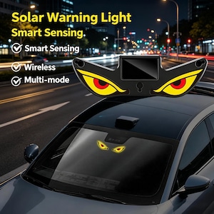 May include: A black solar warning light with yellow and red eye-shaped accents is mounted on a car roof. The text "Solar Warning Light Smart Sensing" is visible. Additional text indicates "Smart Sensing", "Wireless", and "Multi-mode" features.