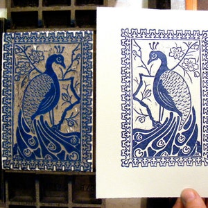 May include: A blue and white print of a peacock with its tail feathers spread out. The print is framed with a decorative border.