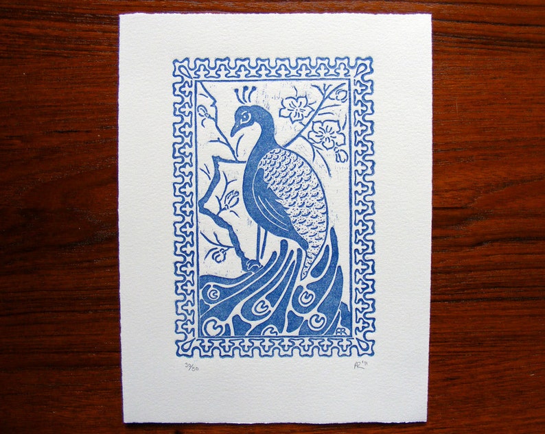 May include: A blue and white print of a peacock with its tail feathers spread out. The print is framed with a decorative border and has the text "39/50" and "R.T." in the bottom corners.