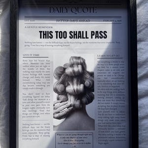 Op de afbeelding: Een zwart ingelijste wandkunstprint ontworpen als een kranteneditie getiteld DAILY QUOTE. De tekst luidt THIS TOO SHALL PASS en bevat kolommen getiteld GIVE IT TIME en LEARN TO LET GO, met een centrale zwart-witfoto van haar in krulspelden.
