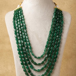 May include: A multi-strand necklace featuring five layers of smooth, oval-shaped emerald green beads. The strands are connected at the top by gold-toned metal caps, creating a cascading effect that rests against the neck with a uniform, polished finish.