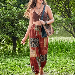 May include: A brown crop top with button details and patchwork pants in shades of red, black, and tan. The pants have a drawstring waist and buttoned cuffs. A brown tote bag with a graphic print is carried over the shoulder.