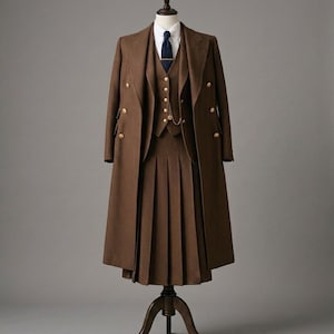 Puede incluir: Un traje de tweed marrón exhibido en un maniquí. El conjunto incluye un abrigo largo, un chaleco, una falda plisada y una camisa blanca con una corbata azul marino. Botones dorados adornan el abrigo y el chaleco. Se ve una cadena de reloj de bolsillo.