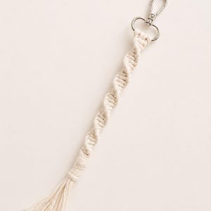 Puede incluir: Llavero de macram&eacute; color crema con cierre plateado. El llavero presenta un dise&ntilde;o de cuerda trenzada y una borla en el extremo. Accesorio hecho a mano para llaves o bolsos.