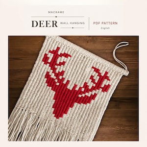 Może przedstawiać: Makrama ścienna w kolorze kremowym z czerwonym wzorem jelenia. Tekst "DEER WALL HANGING" jest wyświetlany nad wzorem. Dolna krawędź ma frędzel.