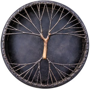 May include: A circular frame drum with a dark, matte black drumhead. A light brown wooden branch is centered on the drumhead, with dark cordage extending from the branch to the outer rim, creating a branching, tree-like pattern across the surface.