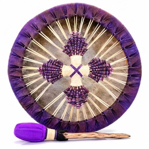 May include: A round frame drum with a purple fabric-wrapped rim and a light-colored drumhead. The center features a cross-shaped design made of small purple beads and light-colored cord. A matching drum mallet with a purple head is included.
