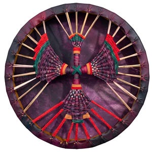May include: A circular drum featuring a deep purple drumhead stretched over a wooden frame. The center is adorned with a cross-shaped woven design in shades of purple, green, red, and orange, connected to the frame by thin wooden spokes.