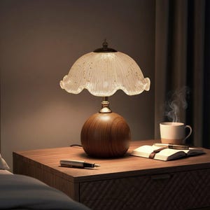 K&ouml;nnte beinhalten: Eine Tischleuchte mit kugelf&ouml;rmigem Holzfu&szlig; und einem geriffelten, durchscheinenden Glasschirm mit goldenen Sprenkeln. Die Lampe steht auf einer Holzoberfl&auml;che neben einem offenen Notizbuch, einem F&uuml;llfederhalter und einer dampfenden Tasse.