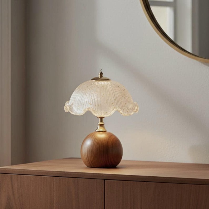 May include: A table lamp featuring a spherical wooden base and a fluted, scalloped glass shade with a gold-toned metal finial and neck. The lamp has a clear, textured glass design that emits a soft glow, supported by a smooth, rounded wood stand.