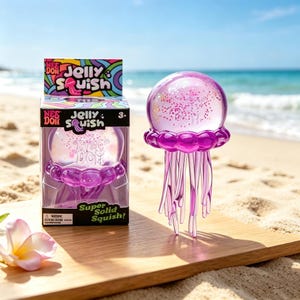 Può includere: Un giocattolo Jelly Squish rosa trasparente a forma di medusa, con base e tentacoli viola. Il giocattolo è esposto su una superficie di legno vicino alla spiaggia. La confezione recita "Jelly Squish!" e "Super Solid Squish!"