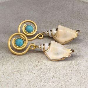 Può includere: Un paio di orecchini color oro con un design a spirale e una pietra rotonda color turchese al centro. Ogni orecchino è fissato a una conchiglia naturale color bianco sporco con dettagli in metallo color oro nel punto di giunzione.