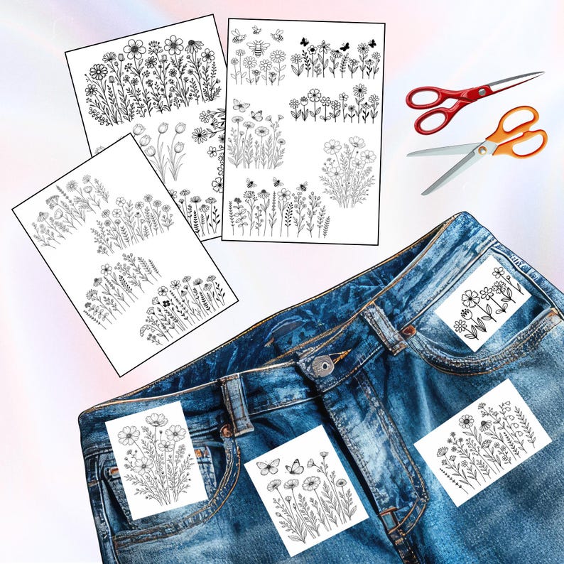 May include: A collection of black and white floral design iron-on patches and paper sheets with various flower and insect illustrations. The patches are placed on a pair of blue denim jeans. Two pairs of scissors are also visible.