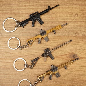 Angled display of four tactical rifle keychains on a wooden background showing different FPS gamer accessory styles.