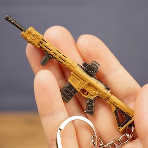 Detailed close-up of tan rifle keychain showing metallic finish, sight, magazine and tactical shooter inspired design.
