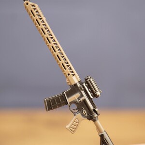 Close-up of tan and black tactical rifle keyring held by fingers, showing long barrel, sight and magazine details.