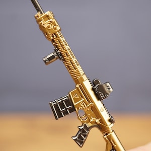 Gold tactical rifle keyring resting in hand with metal key loop, designed as a collectible FPS gamer accessory.