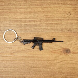 Black tactical rifle keyring with metal chain and key loop on a wooden surface, ideal as an FPS gamer gift.