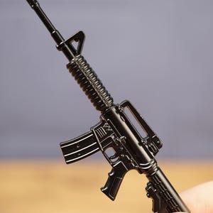 Black miniature rifle keyring held in hand showing classic tactical rifle shape with barrel, magazine and stock detail