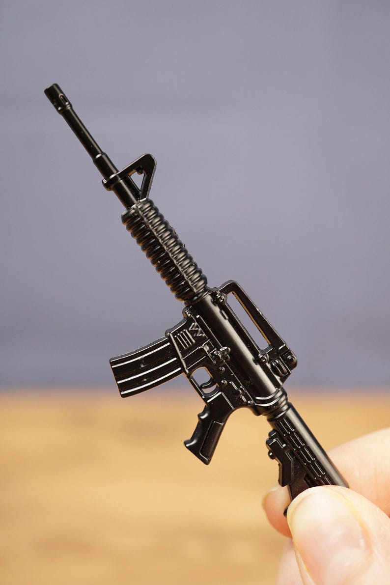 Black miniature rifle keyring held in hand showing classic tactical rifle shape with barrel, magazine and stock detail