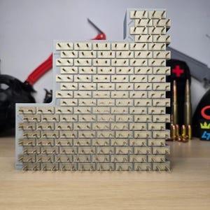 May include: A gray 3D-printed wall display stand featuring a repeating brick pattern. Each individual brick is accented with a small, centered gold-colored metal pin protruding outward, designed for organizing or displaying small items in a grid layout.
