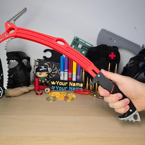 Op de afbeelding: Een rood-zwarte klimijsbijl met een gebogen schacht, een getande houweel en een schoffel aan de bovenkant. Het handvat is zwart met een grijze knop aan de basis. Het gereedschap heeft een opvallend mechanisch ontwerp met zichtbare schroeven en uitsparingen.