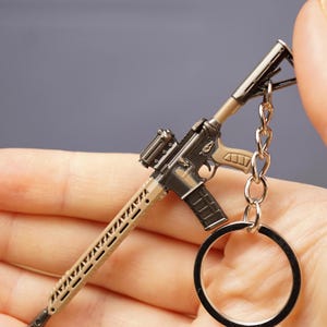 Tan rifle keychain with metal ring displayed in hand, ideal as a battle royale or tactical shooter gamer gift.