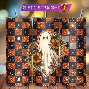 May include: A cylindrical tumbler featuring a checkered pattern of glittery orange and dark blue squares with small stars and ghost icons. The center displays a white ghost surrounded by orange flowers and green leaves. A metal straw is inserted at the top.