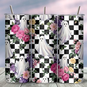 May include: A cylindrical tumbler with a metal straw featuring a repeating pattern of white ghosts, pink roses, yellow flowers, and purple blossoms set against a black and white checkered background. The design wraps around the entire exterior surface.
