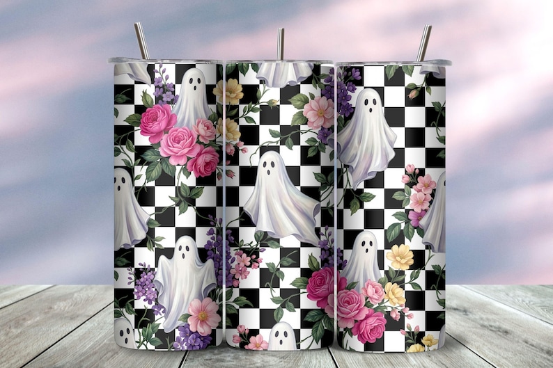 May include: A cylindrical tumbler with a metal straw featuring a repeating pattern of white ghosts, pink roses, yellow flowers, and purple blossoms set against a black and white checkered background. The design wraps around the entire exterior surface.