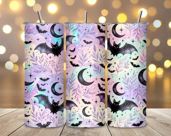 May include: Three cylindrical tumblers with a repeating pattern of black bats, crescent moons, and purple foliage against a pastel iridescent background. Each tumbler features a straight metal straw inserted into the top lid opening.