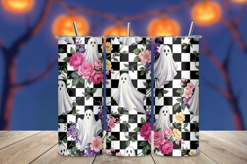 May include: A cylindrical tumbler with a metal straw featuring a black and white checkered pattern overlaid with white ghost illustrations, pink roses, and small purple and yellow flowers. The design covers the entire surface of the drinkware.